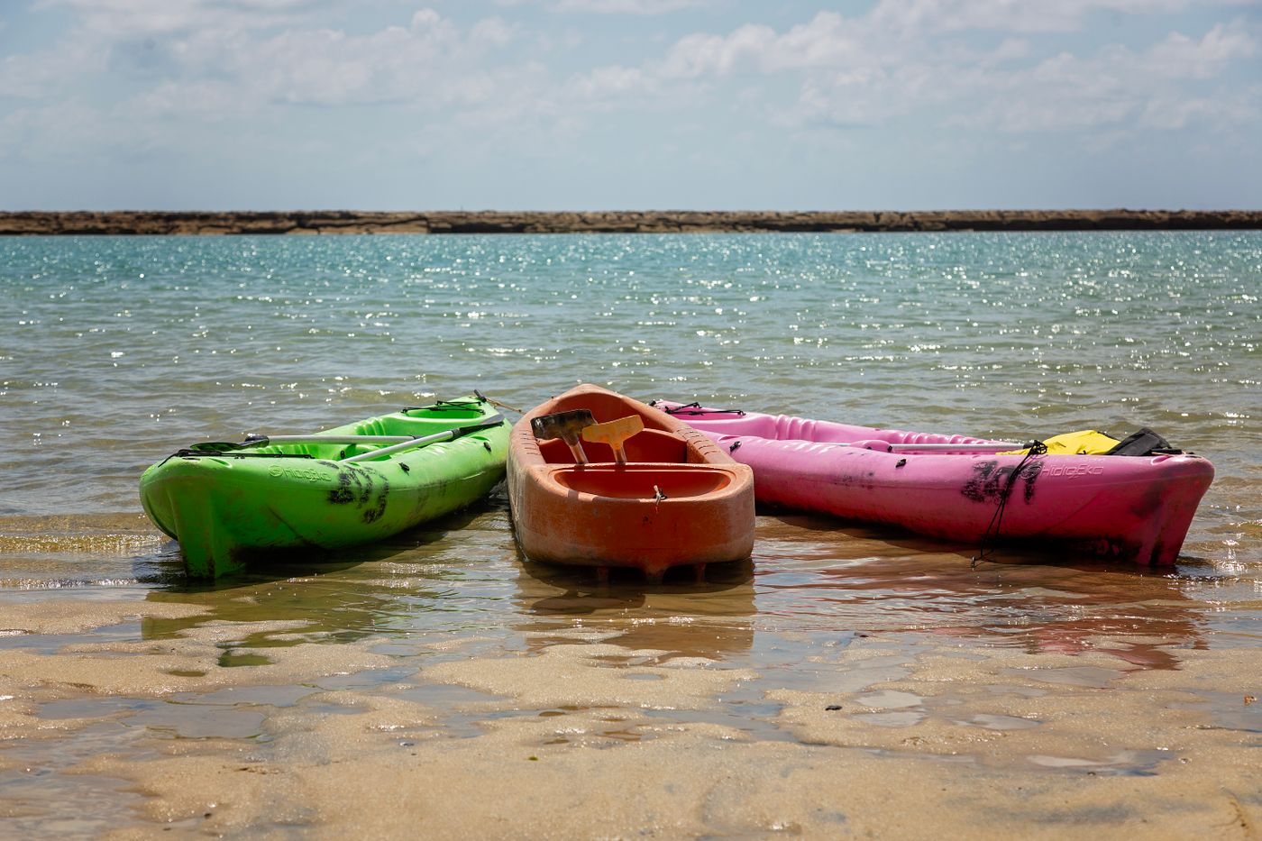 Green, orange and pink kayaks resting in clear turquoise water