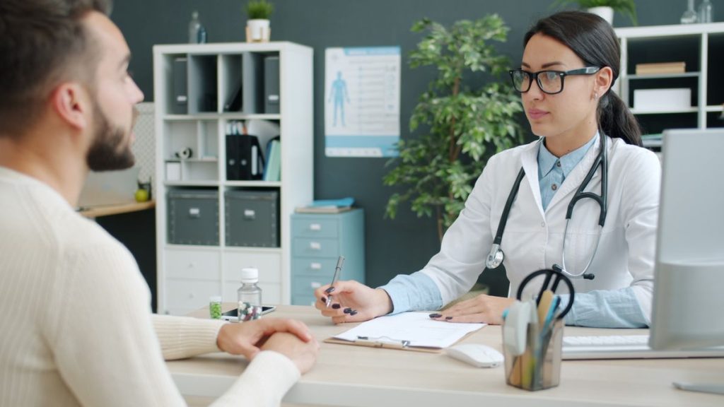 A doctor talking with a patient across a desk in a bright clinic office