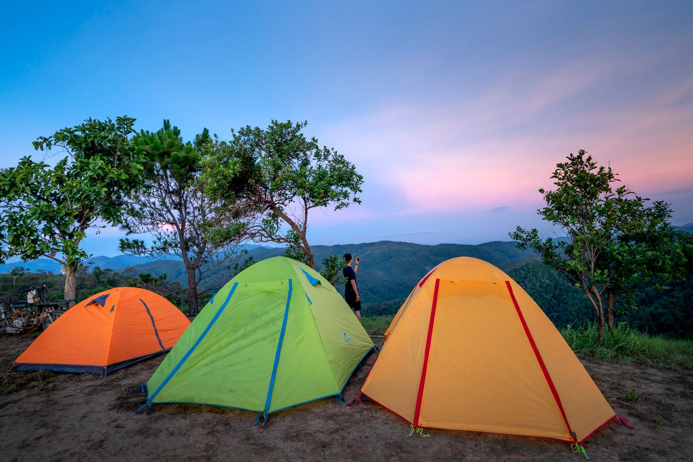 Orange, green and yellow tents pitched on a hilltop at dusk